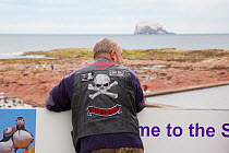 Biker wearing jacket with skull and crossbones emblem looking out over the Firth of Forth towards Bass Rock, North Berwick, Scotland, UK, July 2010