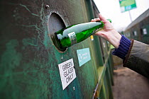 Person putting a glass bottle into a recycling bank at a recycling centre, Stroud, Gloucestershire, UK, February 2008.