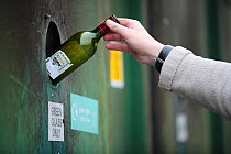 Person putting a green glass bottle into a recycling bank at a recycling centre, Stroud, Gloucestershire, UK, February 2008.