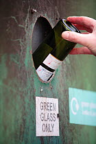 Person depositing a green glass bottle into a recycling bank at a recycling centre, Stroud, Gloucestershire, UK, February 2008.