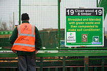 Workman next to infomation sign at wood recycling centre, where wood is made into soil conditioner, Gloucestershire, UK, February 2008.