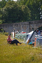 Man relaxing on chair next to his barge, River Thames at Lechlade, Gloucestershire, July 2008.