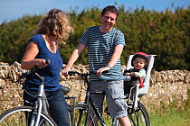 Couple with child resting during a cycle ride in the Cotswolds, Guiting Power, Gloucestershire, UK, August 2011.  Model released