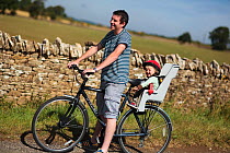 Man with child resting during a cycle ride in the Cotswolds, Guiting Power, Gloucestershire, UK, August 2011. Model released