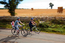 Couple with child in seat cycling in the Cotswolds at Guiting Power, Gloucestershire, UK, August 2011. Model released