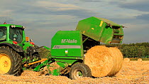 Side view of tractor and baler dumping a bale of Barley straw, before driving away on arable farmland, Inverness-shire, Scotland, UK, September 2011