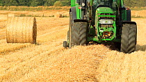 Tractor pulling a baler towards camera, baling Barley (Poaceae sp.) straw on arable farmland, Inverness-shire, Scotland, UK, September 2011