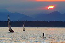 Woman paddleboarding with sailboats in the waters of Puget Sound with the Olympic Mountains in the background, Seattle, Washington, USA