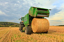 Baling machine ejecting a bale of Barley straw on arable farmland, Scotland, UK, September