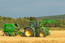Baling machine and tractor collecting Barley straw on arable farmland, Scotland, UK, September