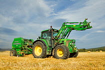 Baling machine and tractor collecting Barley  straw on arable farmland, Scotland, UK