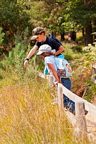 Children looking for wildlife and pointing from the edge of a track, Arne RSPB reserve, Dorset, England, UK, September. Model released.