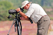 Birdwatcher looking through a telescope for visiting Osprey, Arne RSPB reserve, Dorset, England, UK, September. Model released.