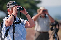 Birdwatchers looking through binoculars for visiting Osprey, Arne RSPB reserve, Dorset, England, UK, September. Model released.