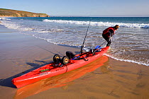 Man dragging fishing kayak into the sea, Praa Sands, Cornwall, England, UK, April 2011