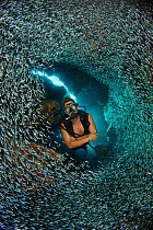 Diver swimming through dense school of Silversides (Atherinidae)  inside a coral cavern, Grand Cayman, Cayman Islands, British West Indies, Caribbean Sea. Model released