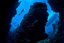 A diver and dive boat visible through the canyons of a coral reef, East End, Grand Cayman, Cayman Islands, British West Indies, Caribbean Sea, January 2011.