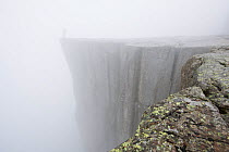 Person standing on Pulpit Rock, 604 meters above the Lysefjorden covered in mist, Rogaland, Norway