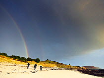 Rainbow and rain clouds over people walking on Par Beach, St. Martin's, Isles of Scilly, UK, 1st January 2012.