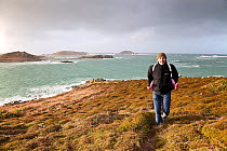 Man carrying child along footpath on a stormy day on St. Martin's, Isles of Scilly, UK, January 2012. Model released.