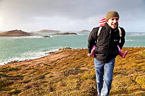 Man carrying child along footpath on a stormy day on St. Martin's, Isles of Scilly, UK, January 2012. No release available.