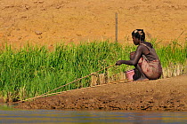 Malagasy woman sitting fishing from the river bank, Tsiribihina River, Madagascar 2008.