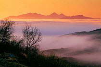 Islands of Rum and Eigg in the Inner Hebrides viewed from Ardnamurchan Peninsular through incoming sea fog at sunset, Argyll, Scotland, May 1999