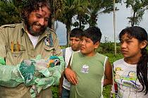 Conservation officer, Hernan Vargas Ayala, examines growing chick from nestbox of Blue throated / Wagler's macaw (Ara glaucogularis) and shows it to group of children, Trinidad, Beni, Bolivia, Critica...
