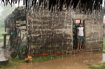 Man standing in doorway of hut in the pouring  rain, Trinidad, Beni, Bolivia, January 2008