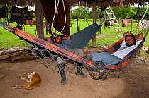 Two men relaxing on hammock in wooden hut, Trinidad, Beni, Bolivia, January 2008