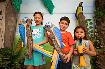 Children with macaw models at the Headquarters of the Programme for the Conservation of the Blue throated / Wagler's macaw (Ara glaucogularis) Trinidad, Beni, Bolivia, Critically endangered species, J...