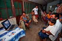 People gathered in front of laptop computer watching an educational programme on the conservation of the Blue throated / Wagler's macaw (Ara glaucogularis) Santa Ana del Yacuma, Beni, Bolivia, Critica...
