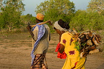 Man and woman in Ishaqbini Reserve, returning from fetching fire wood. Man carrying axe, woman the wood.  Kenya, 2009.