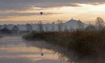 Hot air balloon over the Somerset Levels at dawn, near Glastonbury with Glastonbury Tor in the background, Somerset, UK, October 2011.