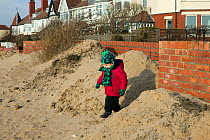 Child playing in sand blown by high winds following poorly planned translocation of sand dune by local authority causing threat to community,  Merseyside, UK 2012