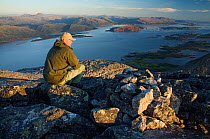 Man sitting on rock overlooking Rodoy (Tro) from Kvasstinden (top of one of the Seven Sisters / De Syv Sostre) Alstahaug, Helgeland, Nordland, August 2007, model released