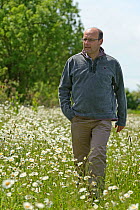 Farm manager, Chris Bailey, walking through herb-rich conservation margin of Ox-eye daisies (Leucanthemum vulgare) at RSPB's Hope Farm, Cambridgeshire, UK, May 2011,  model released