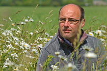 Farm manager, Chris Bailey, walking through herb-rich conservation margin of Ox-eye daisies (Leucanthemum vulgare) at RSPB's Hope Farm, Cambridgeshire, UK, May 2011,  model released