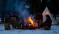 Cowboys sitting round camp fire at dusk, Wyoming, USA, February 2012, model released