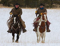 Two mounted cowboys riding in snow, carrying guns, Wyoming, USA, February 2012, model released