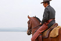 Lusitano horse, man riding stallion beside water, wearing traditional dress, Portugal, May 2011, model released