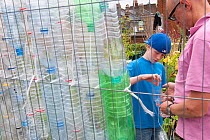 Man and boy making bird scarers from plastic bottles in a community vegetable garden on the roof of Budgens Supermarket, Food from the Sky initiative, Crouch End, London, England, UK, August 2011