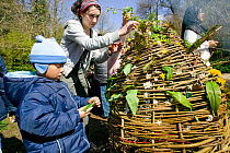 Asylum seeker children decorating whicker easter egg with wildflowers on Easter Sunday to learn about natural world, Wales, April 2009.