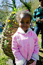 Asylum seeker girl portrait, standing beside whicker easter egg which has been decorated with wildflowers on Easter Sunday to learn about natural world, Wales, April 2009.