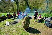 Asylum seeker group sitting around fire in woodlands after decorating whicker easter egg with wildflowers on Easter Sunday, Wales, April 2009.