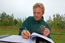 Man holding Great tit (Parus major) while writing notes, birds caught in net for ringing, in an allotment, Grande-Synthe, Dunkirk, France, September 2010, model released