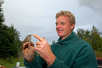 Man holding Dunnock (Prunella modularis) caught in net for ringing, in allotment garden, Grande-Synthe, Dunkirk, France, September 2010, model released