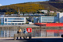 People sitting on bench next to new marina development with high cost urban housing in area of former industrial docks, Swansea, Wales, UK 2009