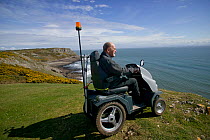 Disabled Man in his 80's enjoying stunning coastal scenery from Pennard cliff using 'Tramper ' machine designed to aid mobility to difficult places for disabled people, Gower, South Wales, UK 2009