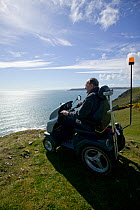 Disabled Man in his 80's enjoying stunning coastal scenery from Pennard cliff using 'Tramper ' machine designed to aid mobility to difficult places for disabled people, Gower, South Wales, UK 2009